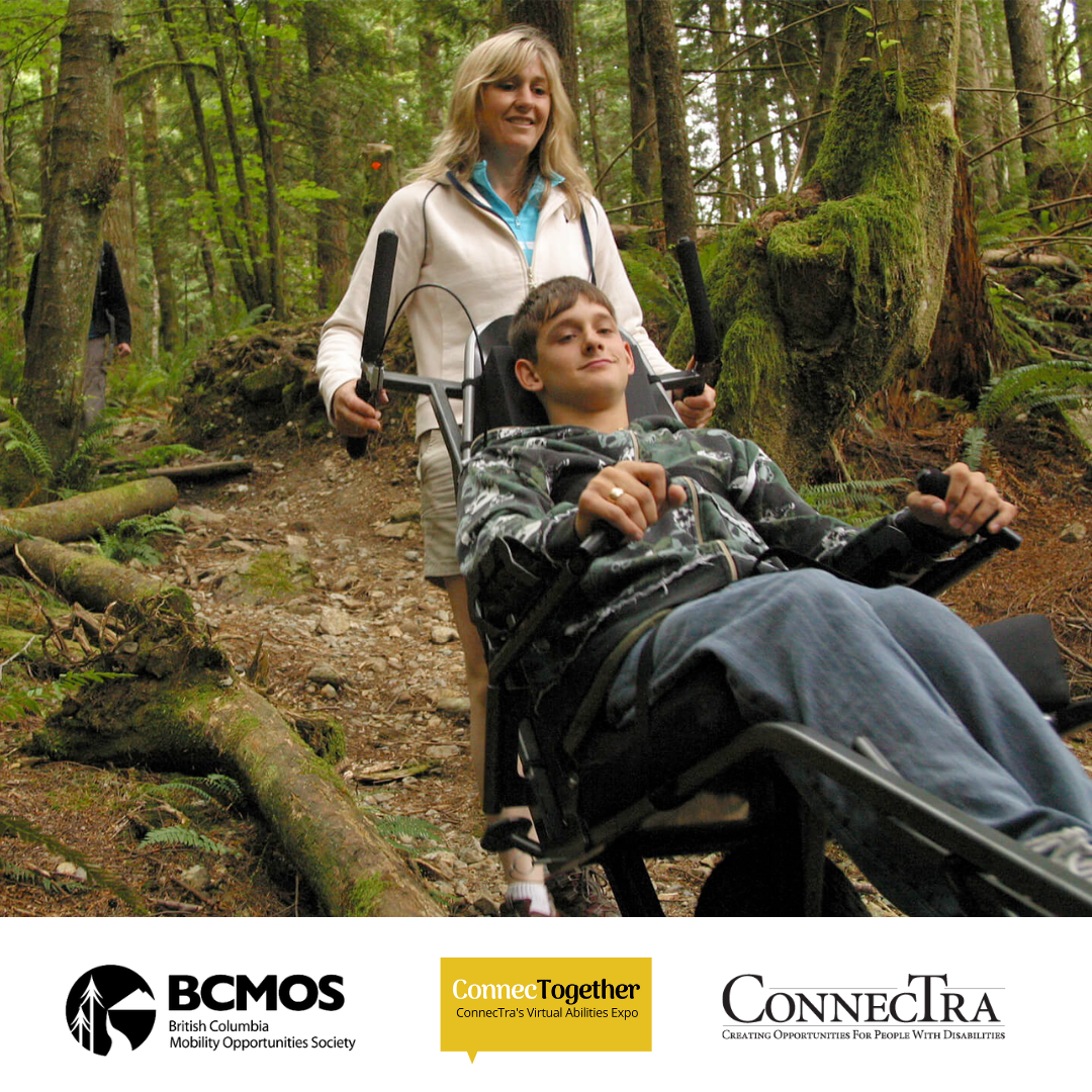 Woman pushes boy in a wheelchair along a trail in the woods as they both smile.