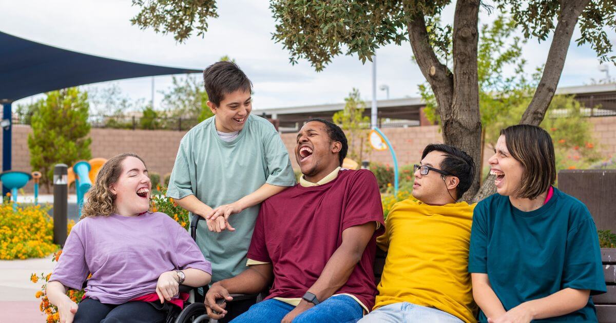 A group of young adults with disabilities engaging in a conversation and laughing in a park.