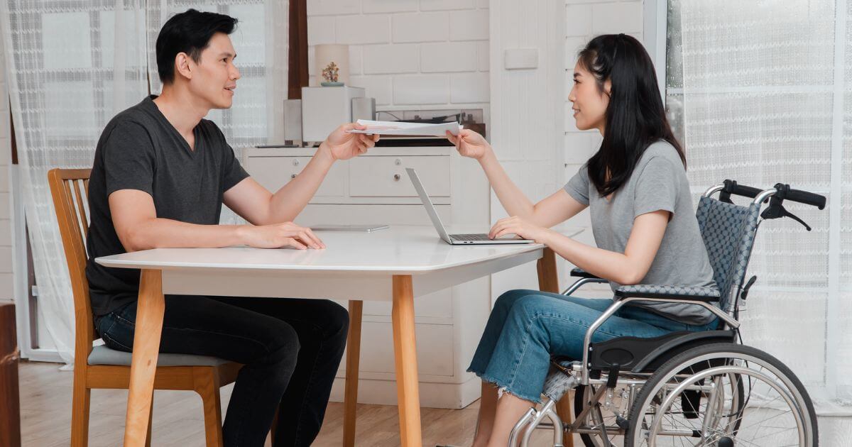 A young woman in wheelchair chatting with her colleague in the office.