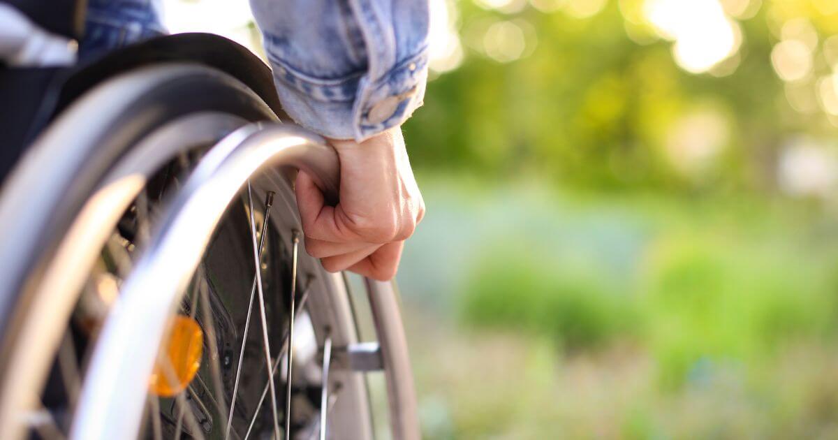 A close-up of a wheel on a wheelchair outdoors.