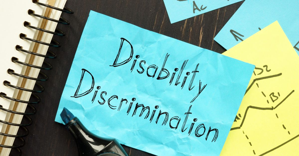 "Disability Discrimination" written on a piece of paper on top of a black, spiral notebook.